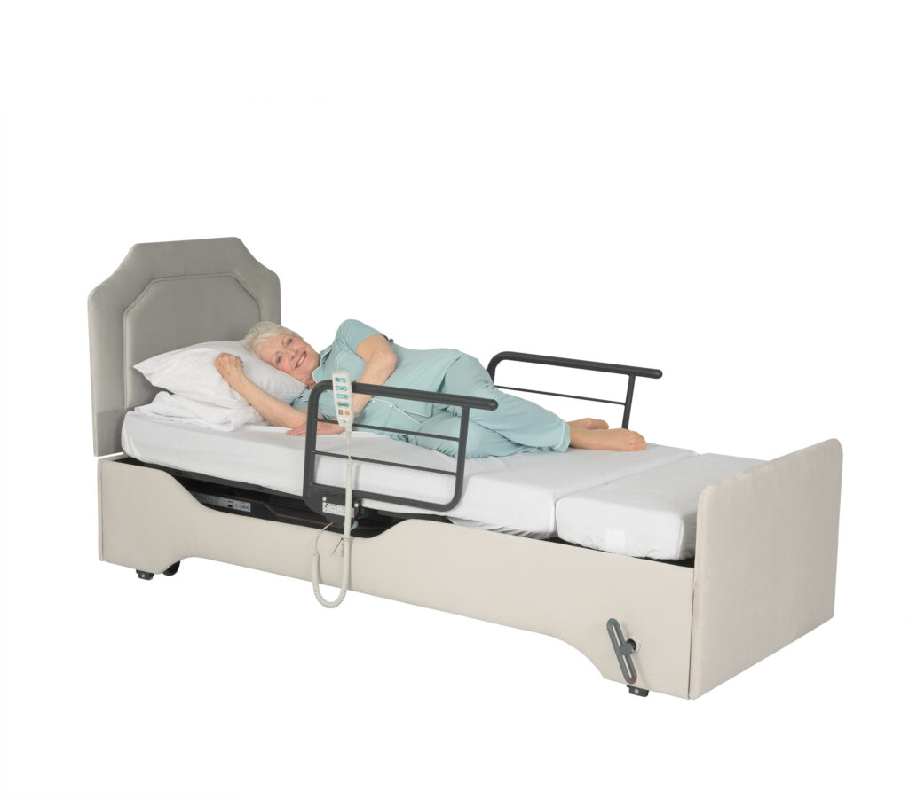 Woman laying flat in a height adjustable electric bed with backrest and bed platform lowered and hand control on the side support handle